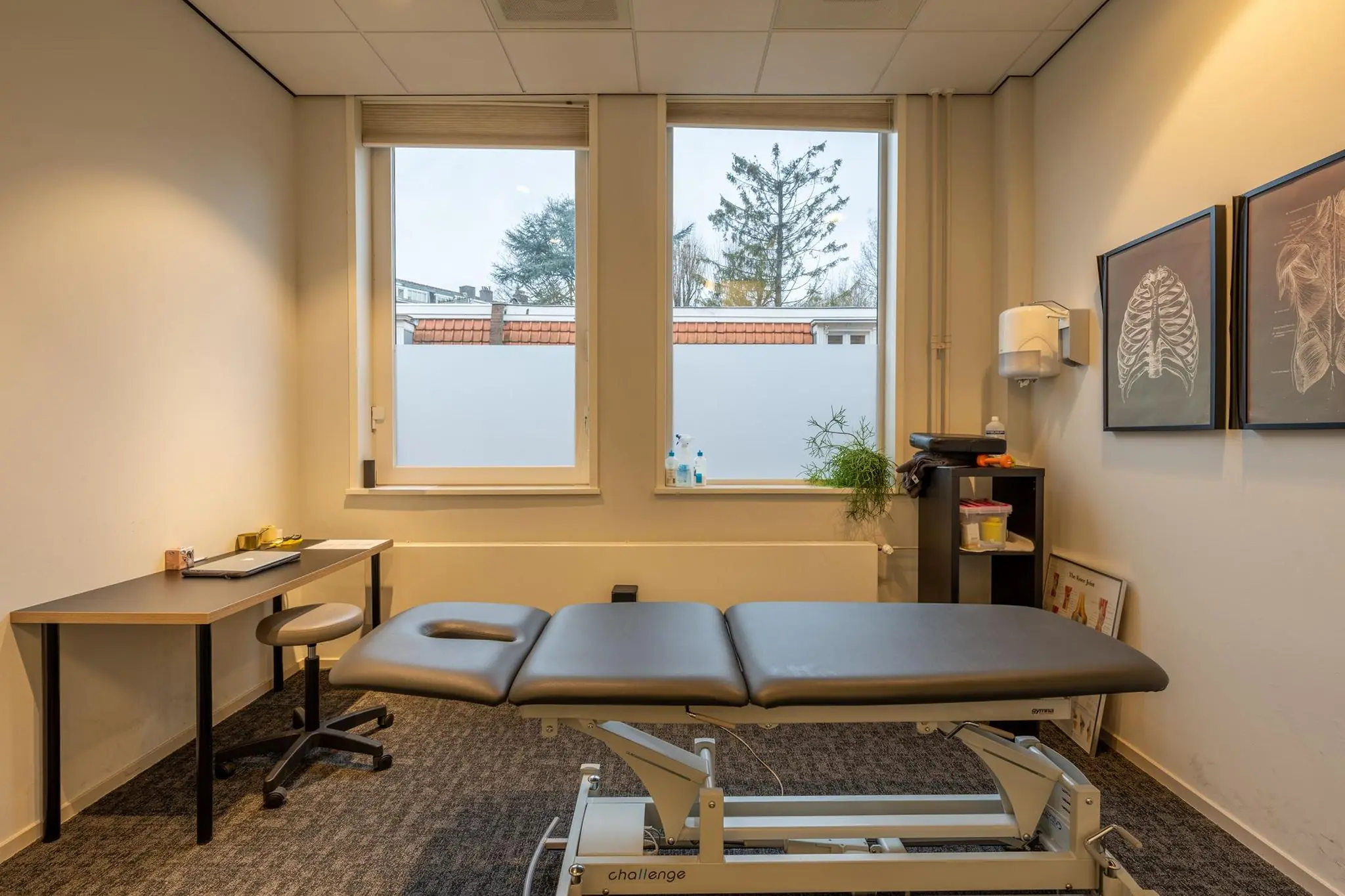 Behandelkamer aan de Admiraal de Ruijterweg met een behandelbank, bureau en anatomische posters aan de muur.